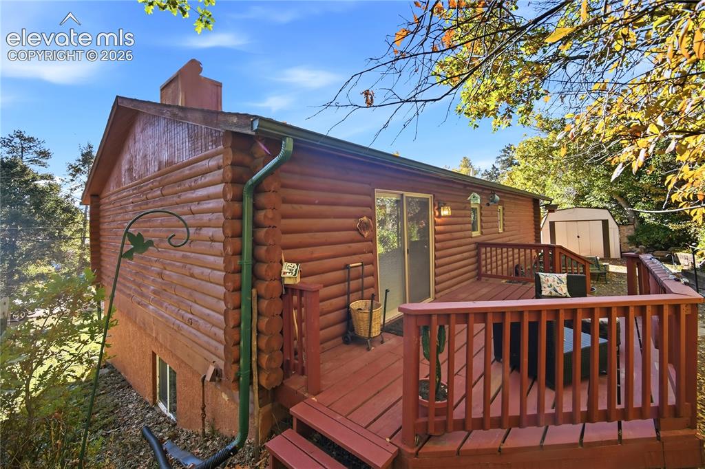 Image 26 of 34: Log cabin exterior with a multi-level wood deck, sliding glass door access,