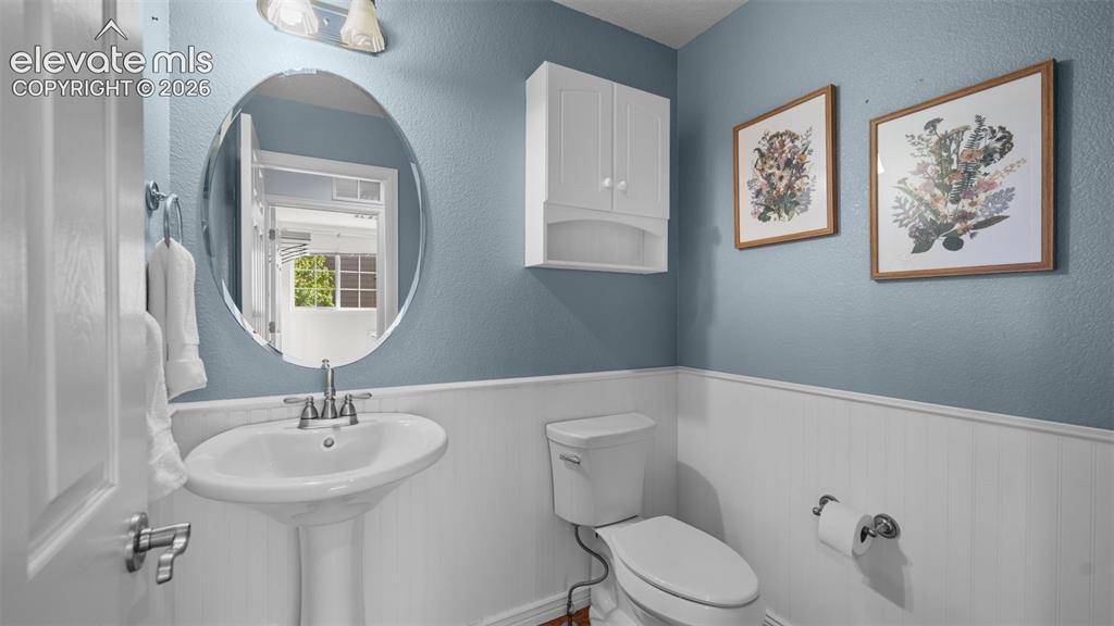 Image 21 of 43: Pedestal sink with chrome faucet, framed by an oval mirror, and white wains