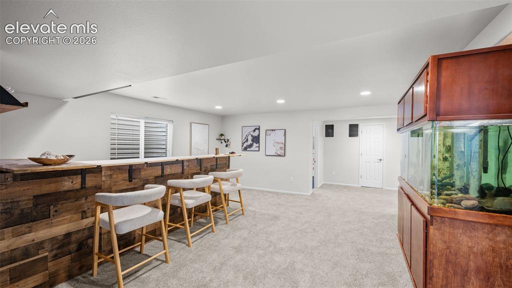 Image 29 of 43: Basement recreation room featuring a custom wood-plank bar, recessed lighti