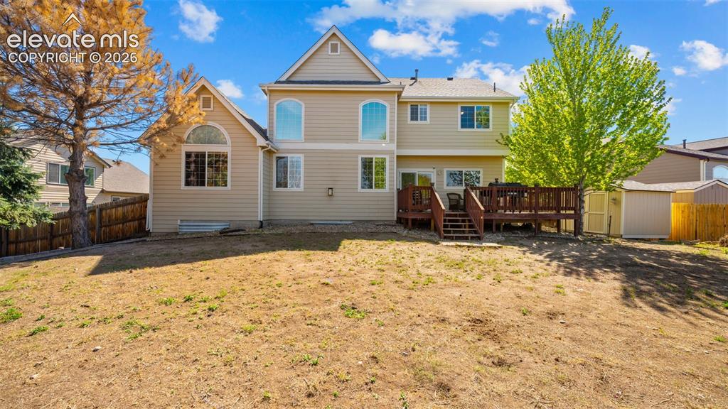 Image 36 of 43: Rear exterior featuring tan siding, a brown multi-level deck, multiple arch
