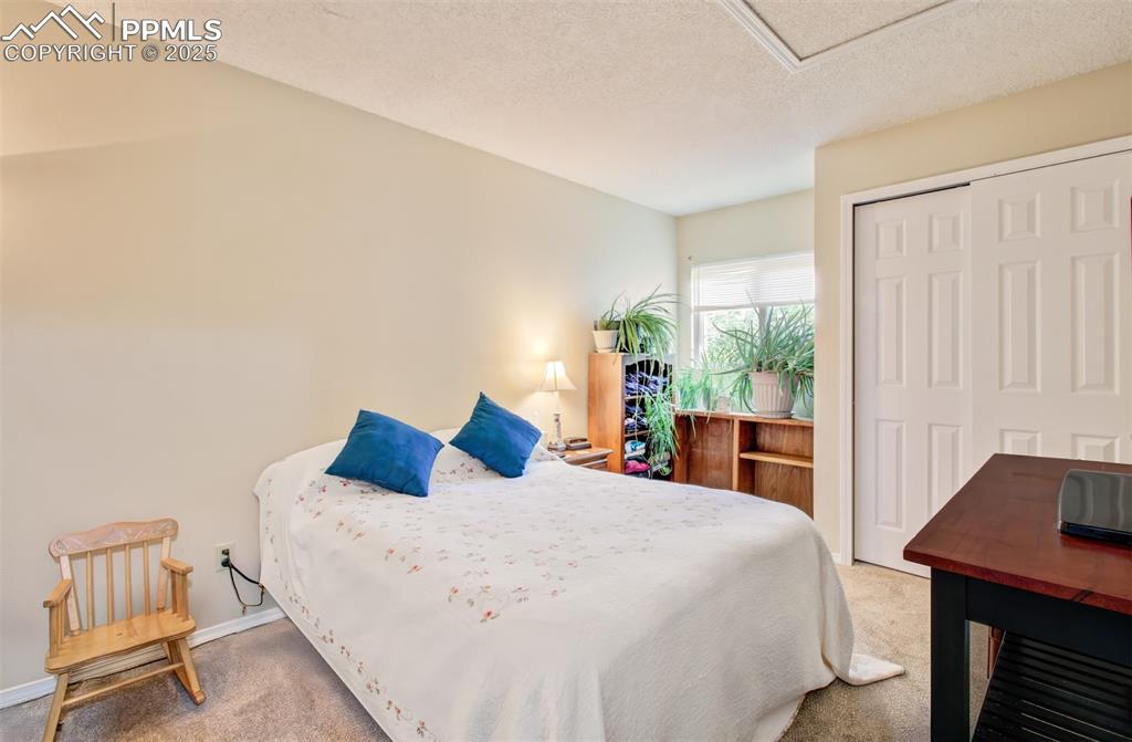 Image 12 of 25: Bedroom with carpet flooring, a closet, a textured ceiling, and attic acces