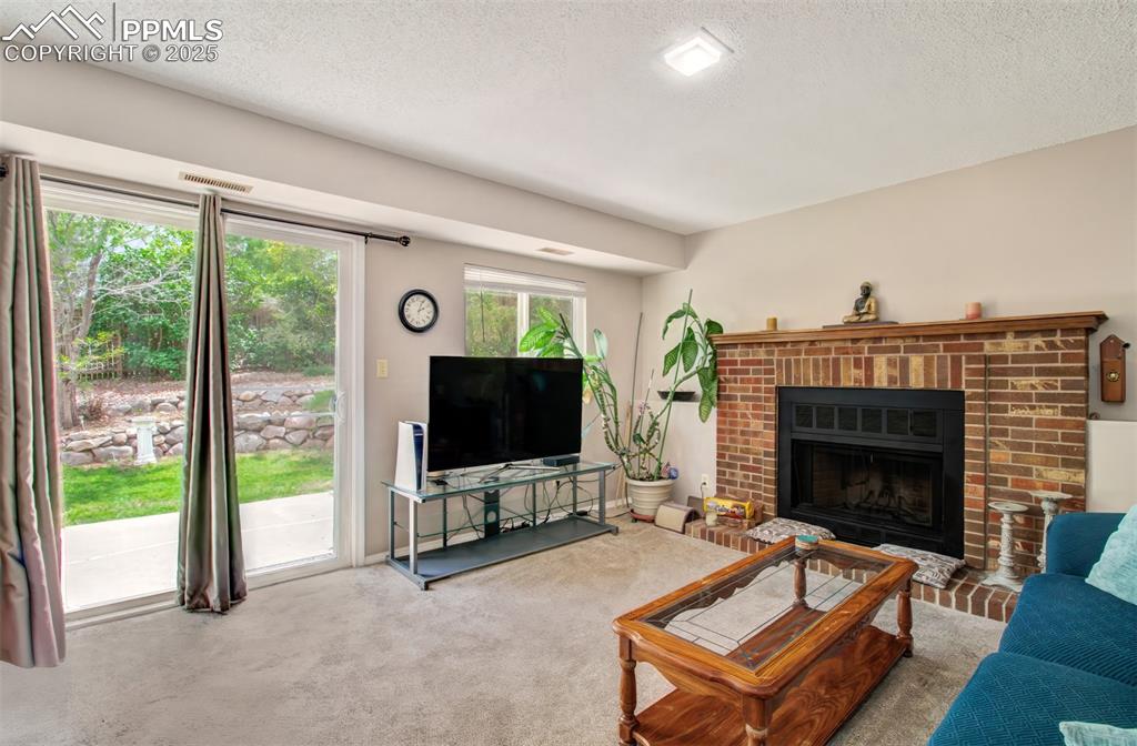 Image 6 of 25: Living area with a textured ceiling, carpet floors, and a brick fireplace