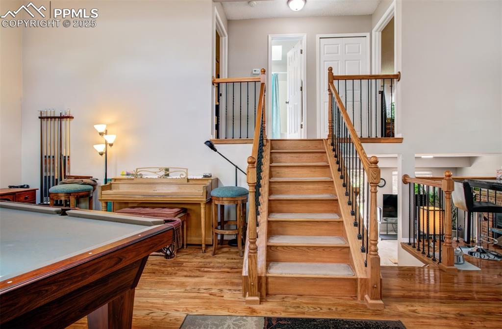 Image 8 of 25: Staircase with wood finished floors and pool table
