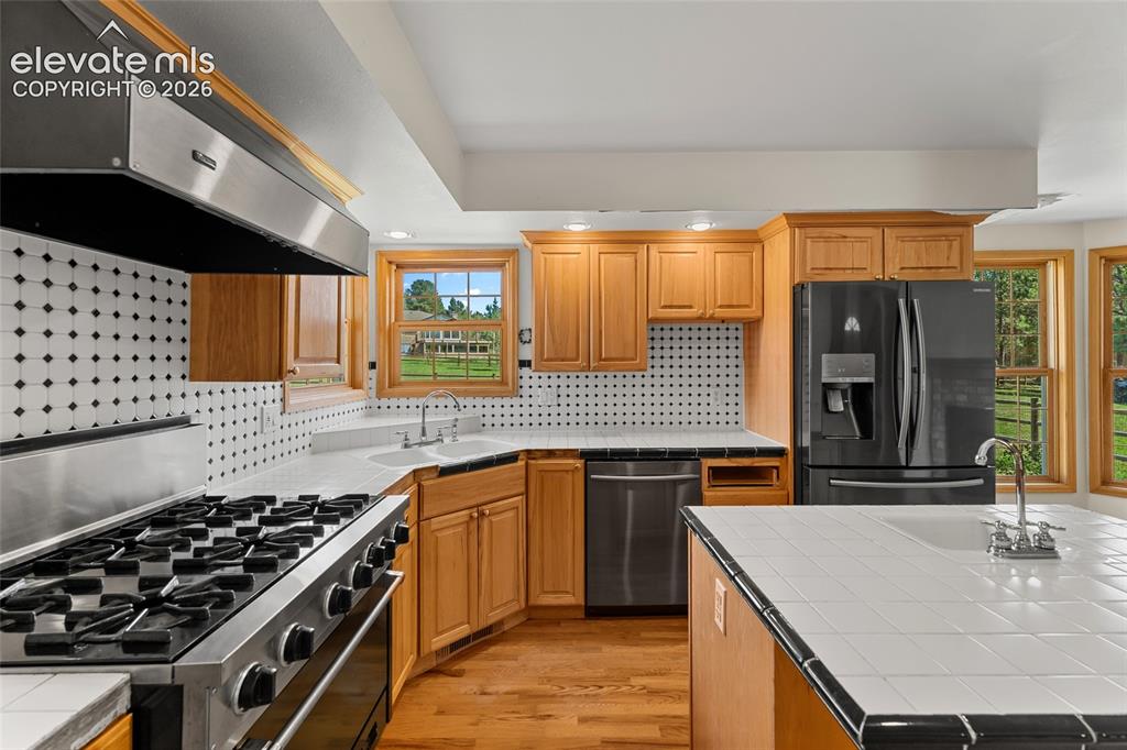 Image 11 of 49: Kitchen featuring wood cabinetry, stainless steel range with hood, black ap