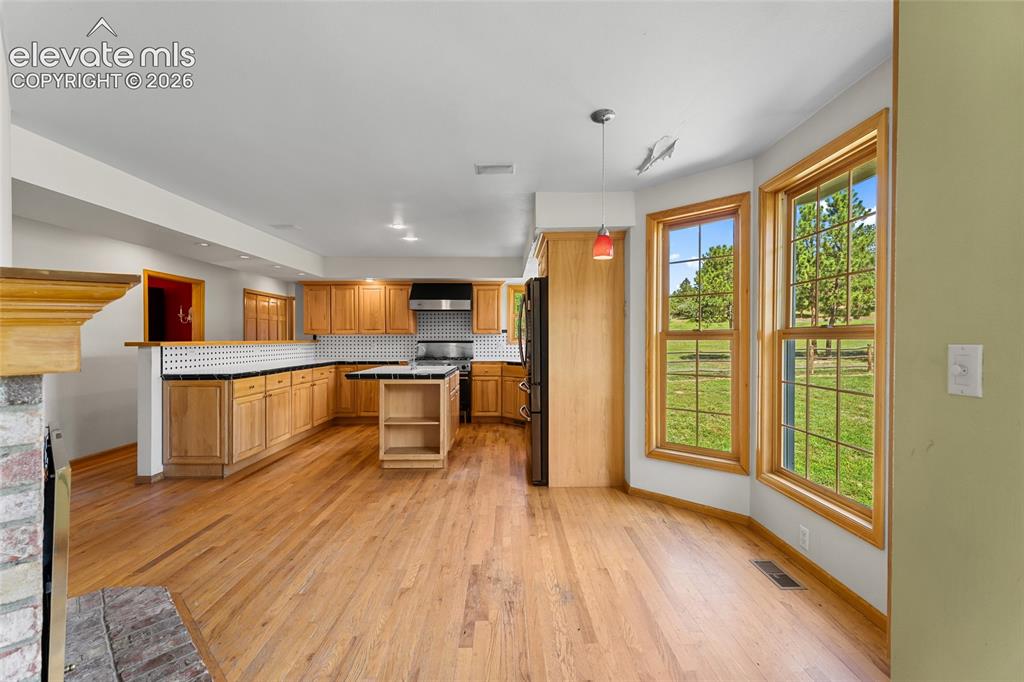 Image 13 of 49: Kitchen with wood-finish flooring, light wood cabinetry, and a black and wh