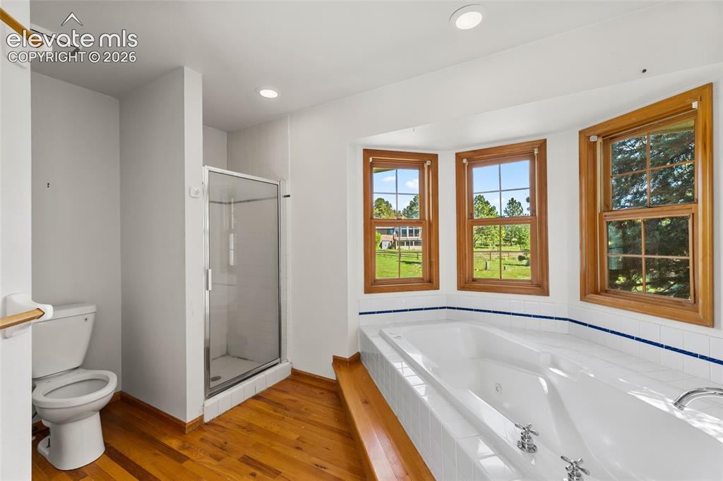 Image 35 of 49: Soaking tub with tile surround, wood-finish flooring, three windows with wo