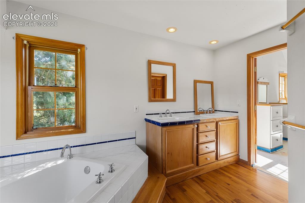 Image 36 of 49: Corner soaking tub with tiled surround, wood-frame window, dual vanity with