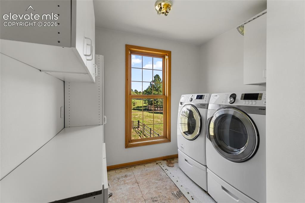 Image 42 of 49: Laundry area featuring white cabinetry, a wood-framed window, and a flush m