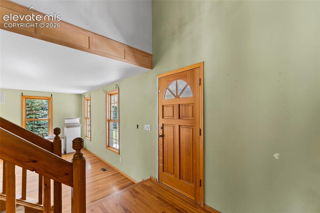 Image 6 of 49: Natural wood door with an arched transom, hardwood flooring, and light gree