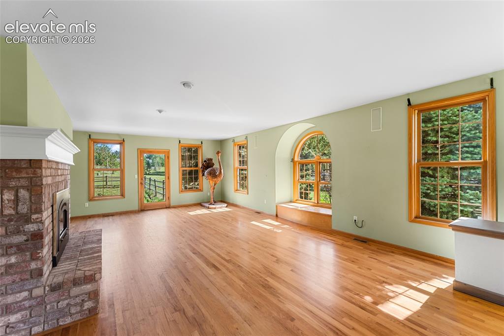 Image 7 of 49: Brick fireplace with a white mantel, wood-finish flooring, multiple windows