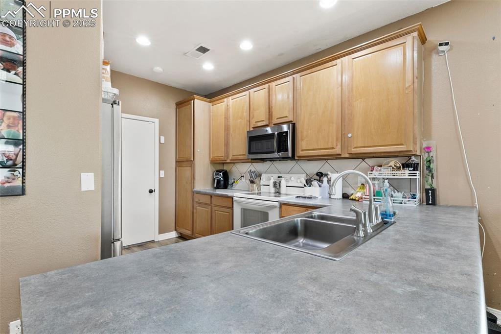 Image 13 of 29: Kitchen featuring backsplash, appliances with stainless steel finishes, lig