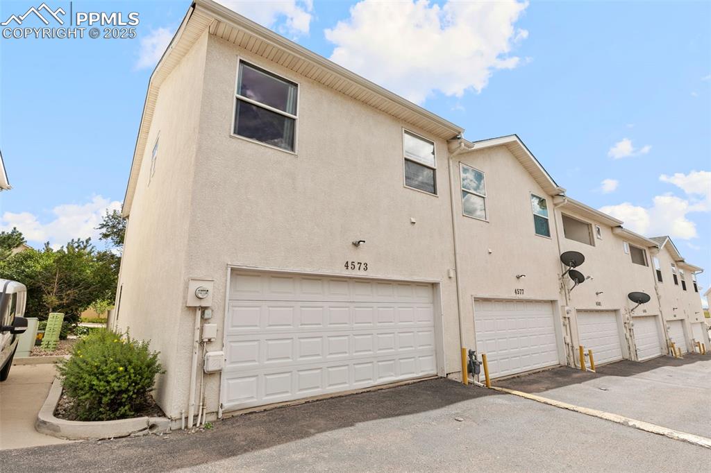 Image 29 of 29: Rear view of property featuring stucco siding, an attached garage, and driv