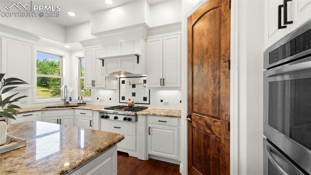 Image 11 of 50: Kitchen with white cabinets, light stone countertops, decorative backsplash