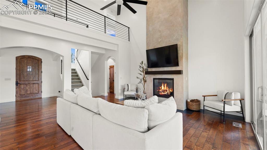 Image 22 of 50: Living room with arched walkways, a towering ceiling, dark wood-type floori