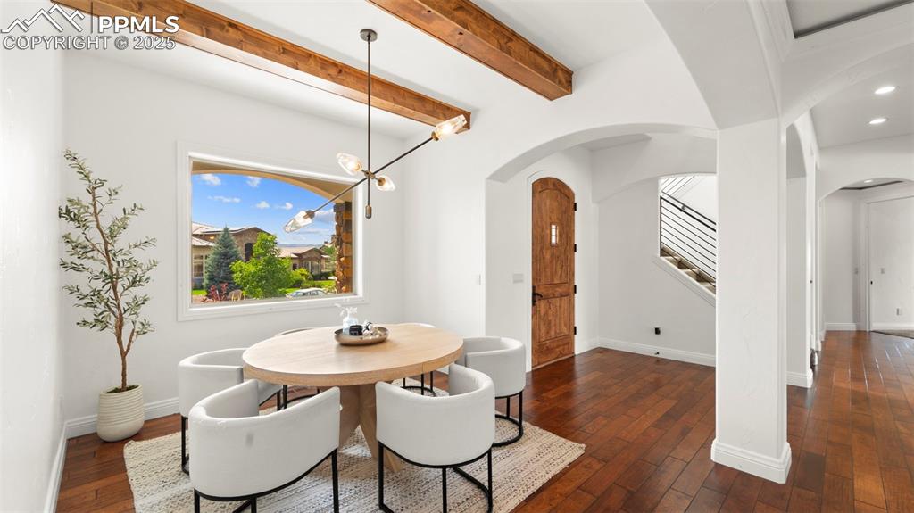Image 6 of 50: Dining area with a chandelier, dark wood-type flooring, stairway, beam ceil