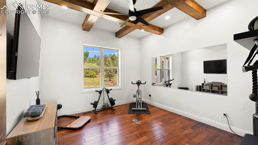 Image 8 of 50: Exercise area with dark wood finished floors, a ceiling fan, and coffered c