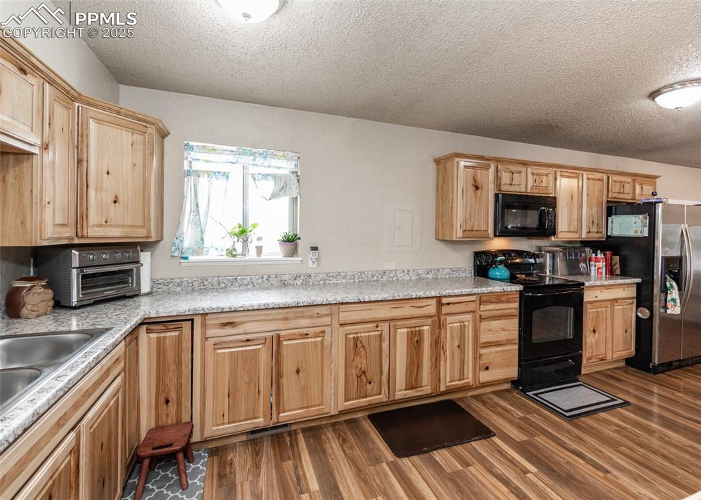 Image 10 of 42: Kitchen featuring black appliances, a textured ceiling, dark wood-style flo