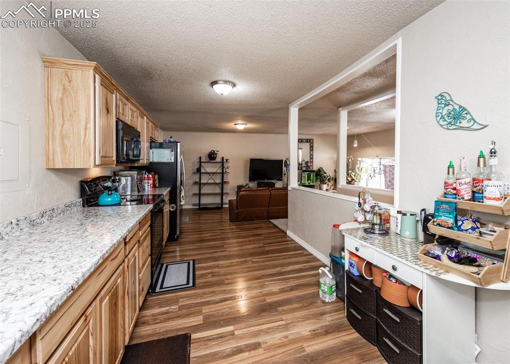 Image 12 of 42: Kitchen with black appliances, a textured ceiling, light wood-style floors,