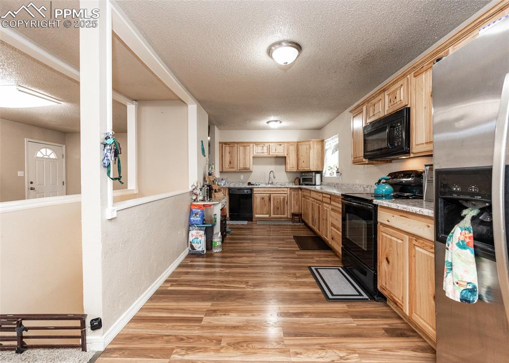 Image 6 of 42: Kitchen featuring black appliances, light brown cabinets, a textured ceilin