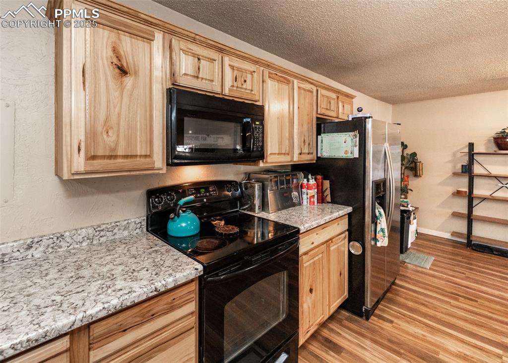 Image 8 of 42: Kitchen featuring black appliances, light brown cabinetry, a textured ceili