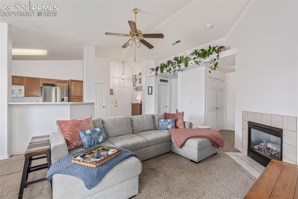 Image 4 of 22: Living area with a ceiling fan, a fireplace, light colored carpet, and high