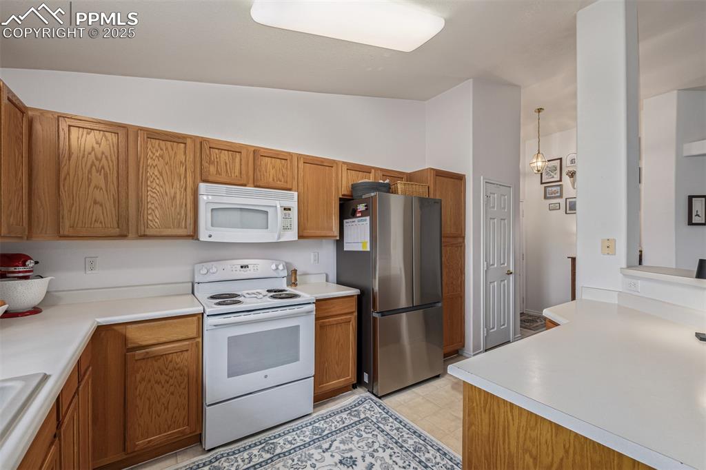 Image 7 of 22: Kitchen with white appliances, brown cabinets, light countertops, and lofte