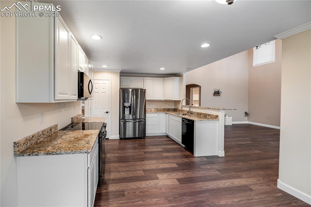 Image 15 of 46: Kitchen with a peninsula, black appliances, arched walkways, dark wood-styl