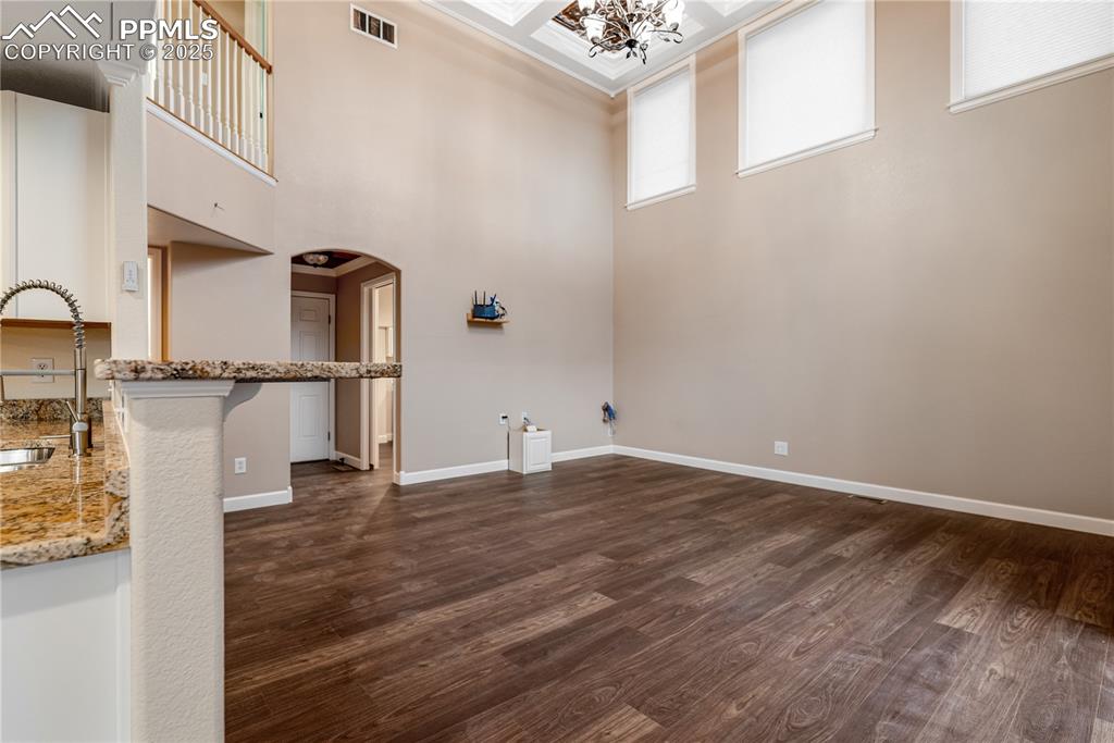 Image 18 of 46: Unfurnished living room featuring a chandelier, arched walkways, dark wood-