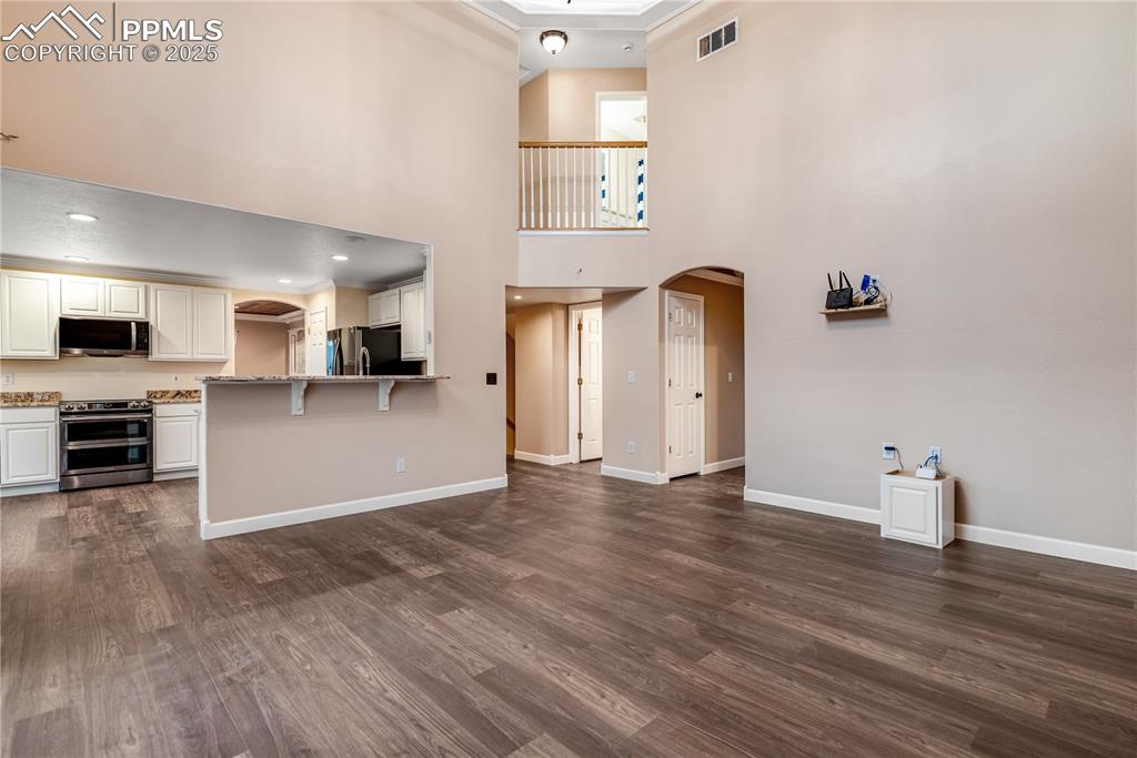 Image 21 of 46: Unfurnished living room with arched walkways, dark wood-type flooring, crow