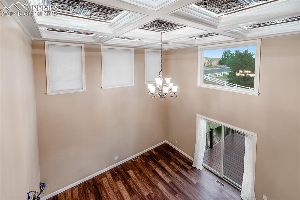 Image 22 of 46: Empty room featuring a chandelier, dark wood-style floors, coffered ceiling