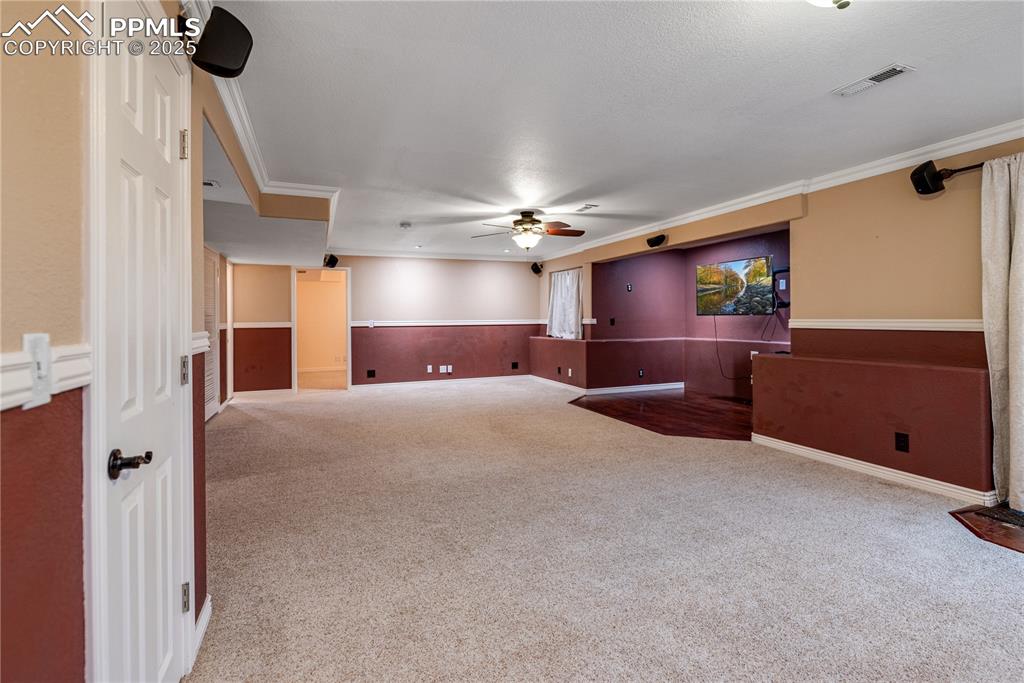 Image 26 of 46: Empty room with a ceiling fan, carpet, crown molding, and wainscoting