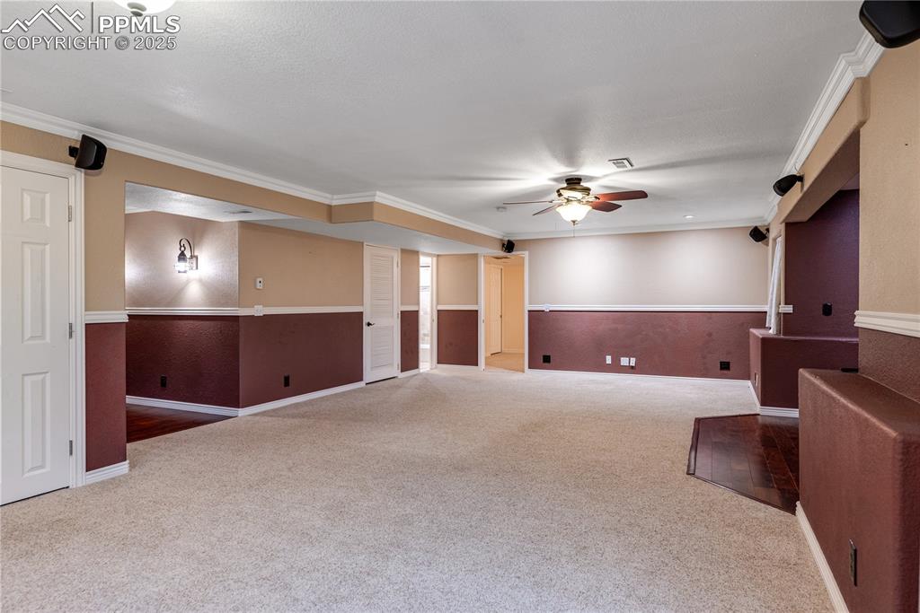 Image 31 of 46: Carpeted empty room featuring a ceiling fan, crown molding, and wainscoting