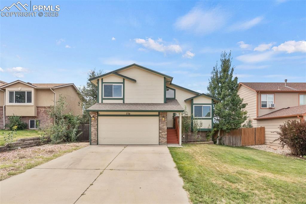 Caption: Tri-level home with an attached garage, concrete driveway, brick siding, and a shingled roof