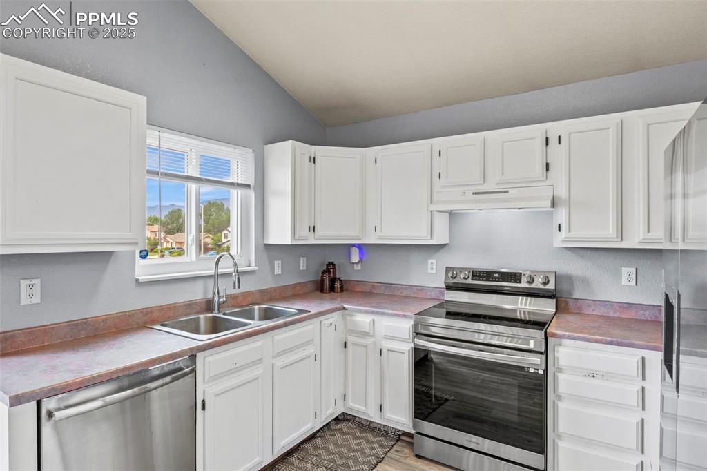 Image 12 of 35: Kitchen with stainless steel appliances, lofted ceiling, white cabinets, un