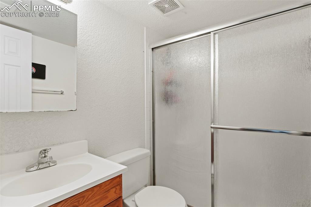 Image 22 of 35: Full bathroom with a textured wall, vanity, a shower with shower door, and