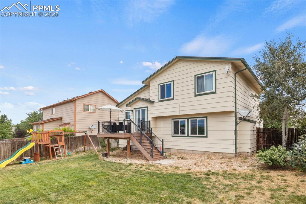 Image 34 of 35: Back of property featuring a fenced backyard, a wooden deck, a playground,
