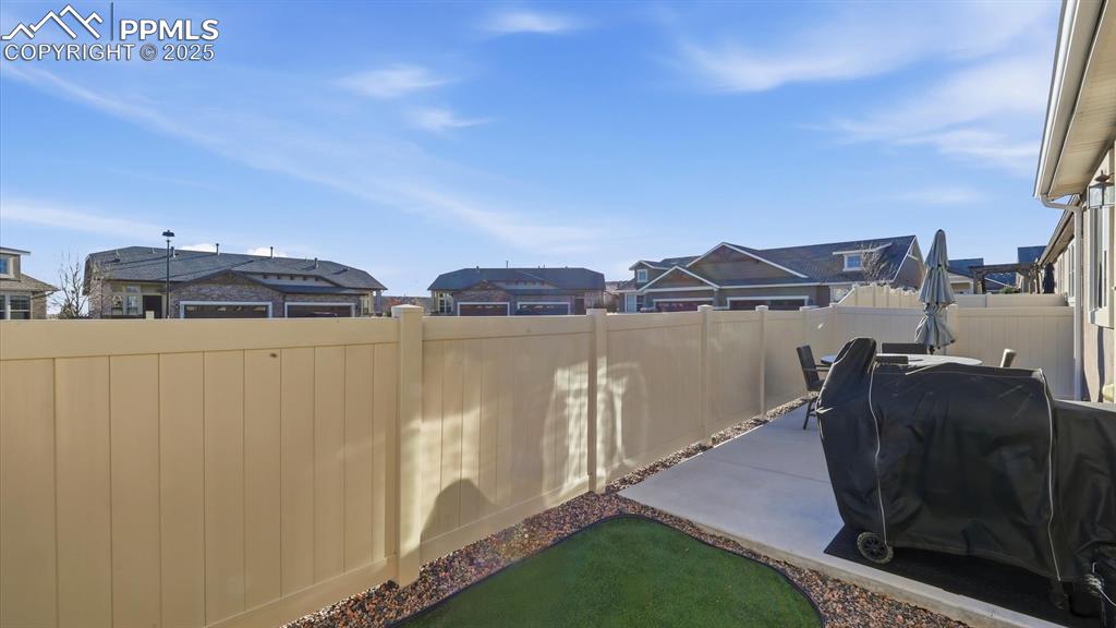 Image 15 of 42: Fenced backyard with concrete patio for outdoor relaxation.