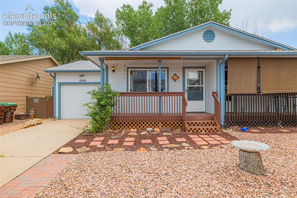 Caption: Front exterior featuring a covered porch, attached garage, and granite xeriscaped landscaping