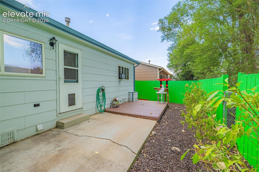 Image 11 of 15: Rear exterior featuring light blue siding, a concrete patio, and a brown wo