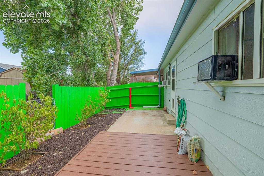 Image 12 of 15: Backyard featuring a wood deck, concrete patio, and a vibrant green privacy