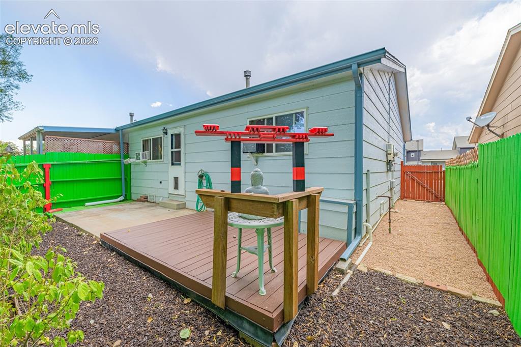 Image 13 of 15: Rear exterior featuring light blue siding, a wood deck, concrete patio, and