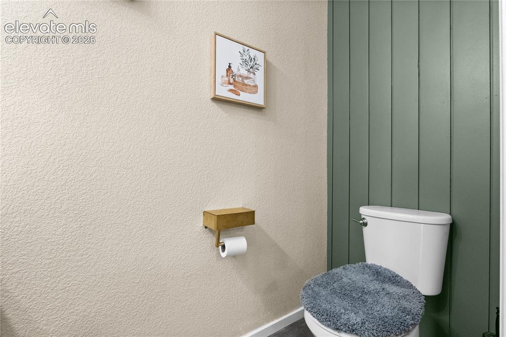 Image 11 of 41: Powder room featuring a white toilet, vertical green paneling, and textured