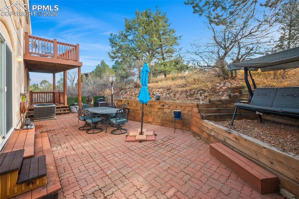 Image 6 of 32: Southwest view of rear patio. Stone wall and brick patio. Rear top deck vis