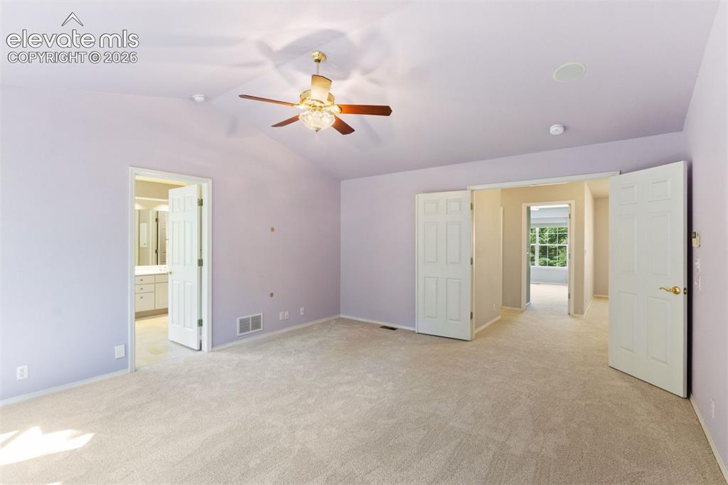 Image 25 of 50: Primary bedroom with vaulted ceiling, french doors, ceiling fan, and ensuit