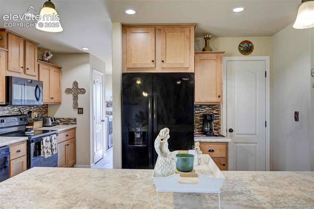 Image 16 of 50: Kitchen featuring light wood-finish cabinetry, black appliances, a tile bac
