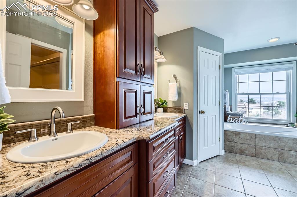 Image 16 of 34: Bathroom with double vanity, a sink, tile patterned floors, and tiled tub