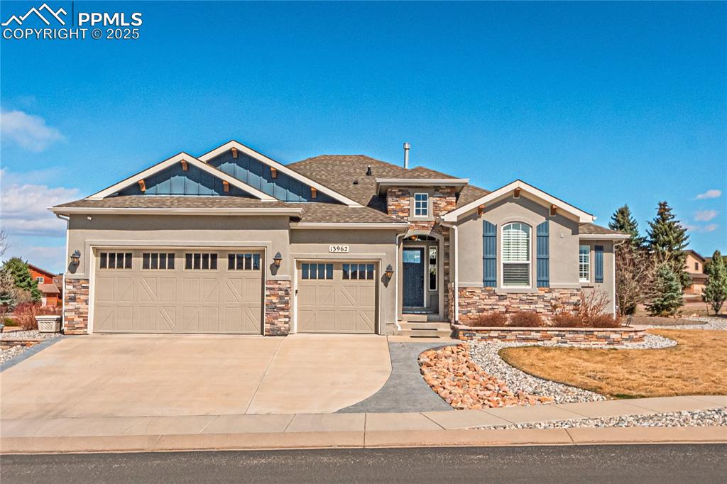 Caption: View of front facade with stucco siding, driveway, stone siding, a shingled roof, and a garage