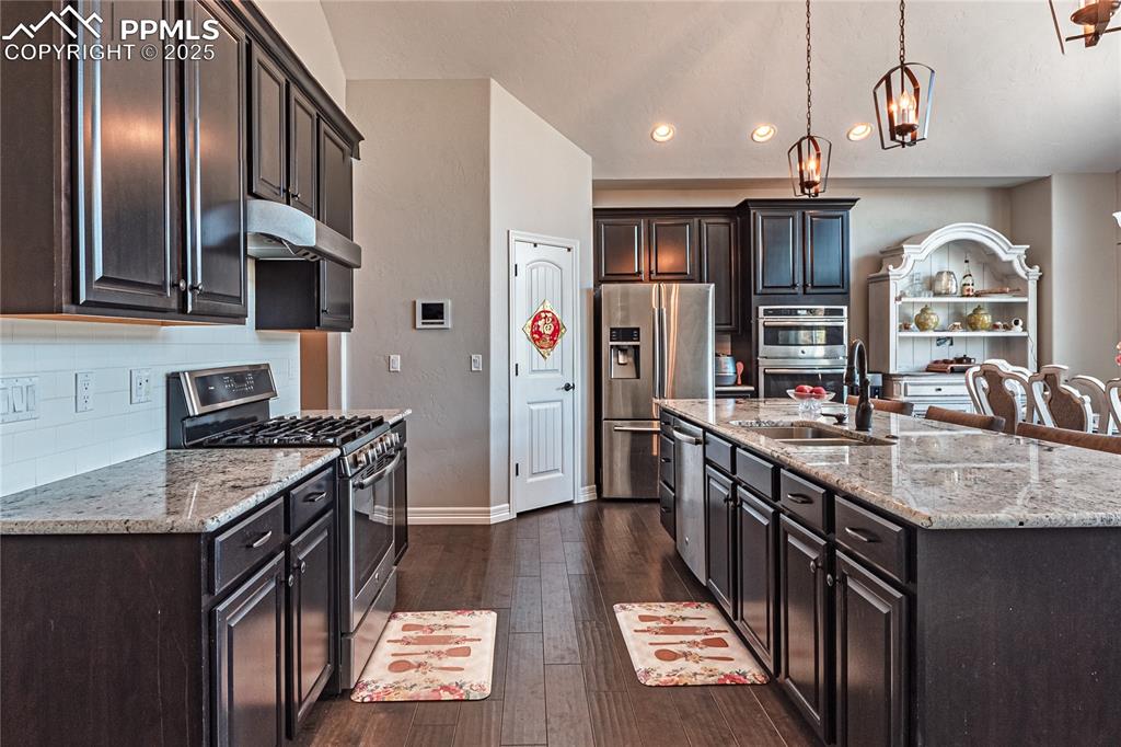 Image 7 of 36: Kitchen with dark wood-type flooring, under cabinet range hood, stainless s