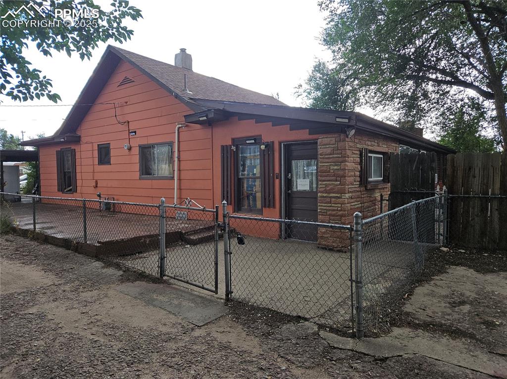 Caption: View of property exterior featuring a gate, a chimney, a fenced front yard, and stone siding
