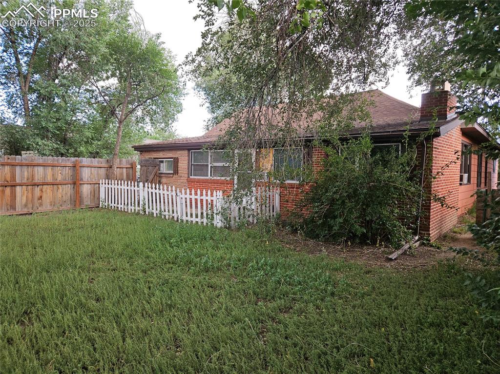Image 3 of 4: Rear view of property featuring brick siding, a chimney, and a shingled roo